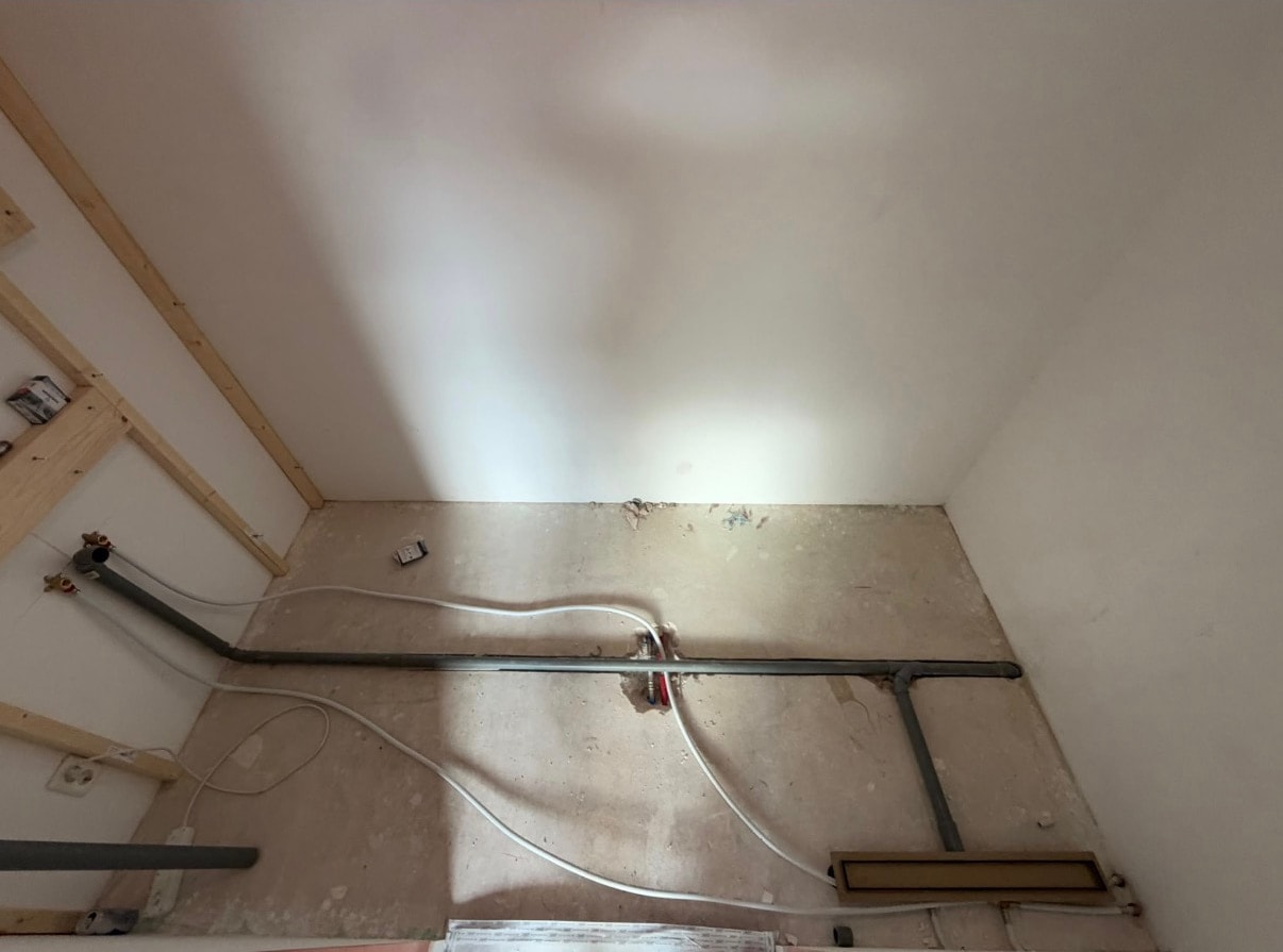 Nieuwe water- en afvoerleidingen op de vloer van een badkamer in aanbouw, met douchegoot