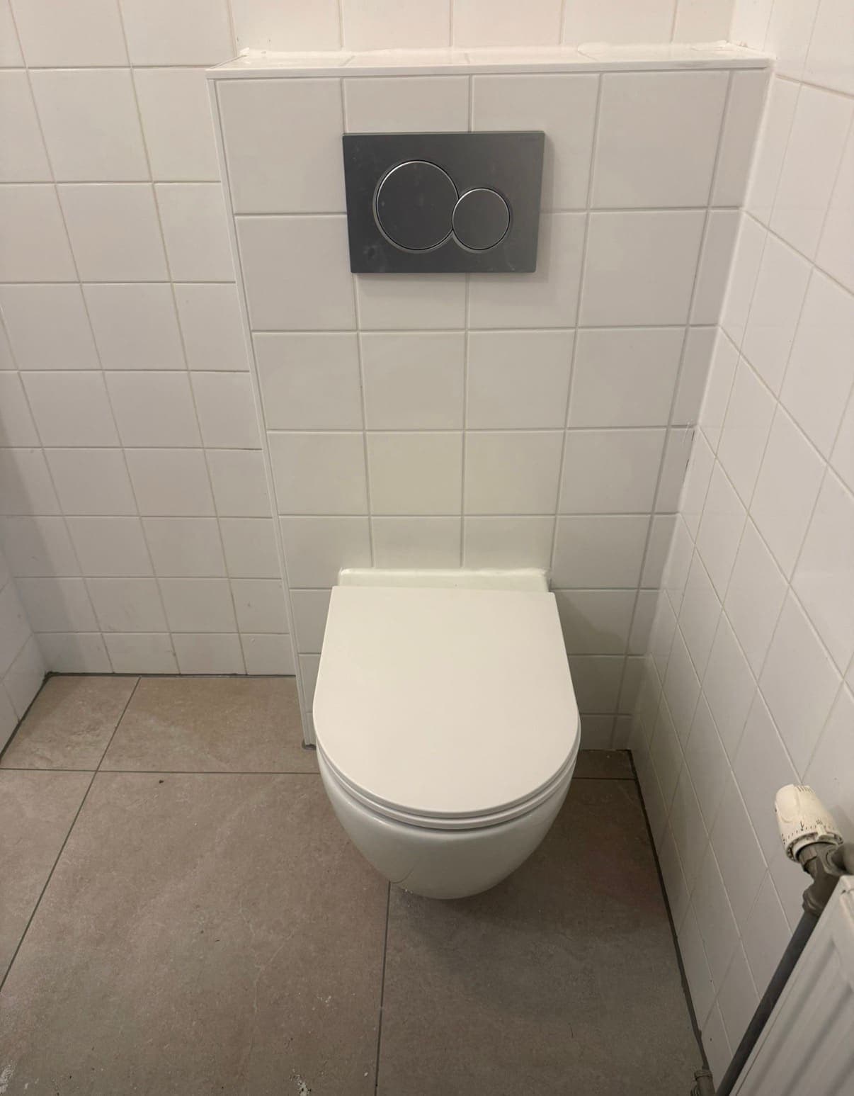 Afgewerkt hangtoilet met bedieningsplaat in een betegelde toiletruimte