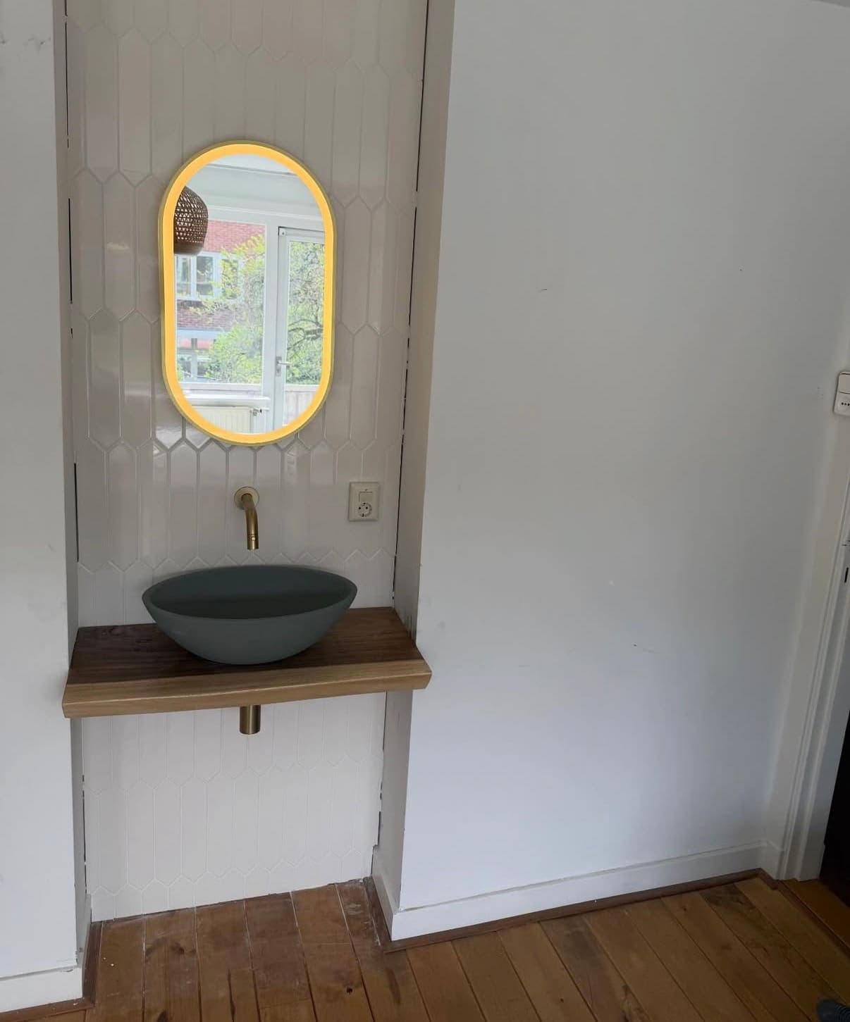 Waskom op een houten blad met verlichte spiegel en gouden kraan
